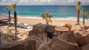 A beachside resort with a view of the ocean, lounge chairs, umbrellas, and a dining area with a patterned table. - Ocean front over looking the arch in Cabo San Lucas, with golf access (Cabo San Lucas)
