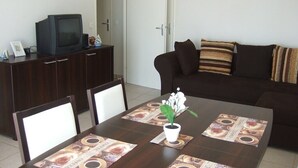 A dining area with a table set for four, a dark brown sofa, and a television on a cabinet. - Beautiful apartment for 4 people (BISCARROSSE)