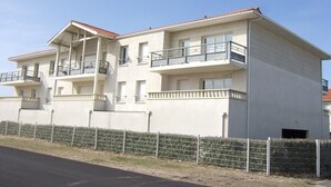 A multi-story building with balconies, a flat roof, and a metal fence in front. - Beautiful apartment for 4 people (BISCARROSSE)