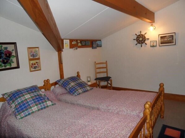 Un dormitorio con dos camas de madera, una silla y un aplique de pared.