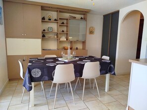 A dining area with a table set for four, surrounded by white chairs. There is a cabinet with shelves above the table, and a mirror on the wall. - Face Lagune superb ground floor flat with parking - 6BAIE12 (SAINT CYPRIEN PLAGE)