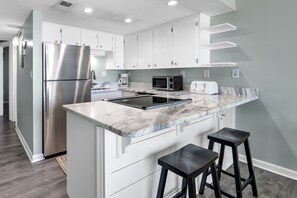 A modern kitchen with white cabinetry, a stainless steel refrigerator, a microwave, and a marble countertop.