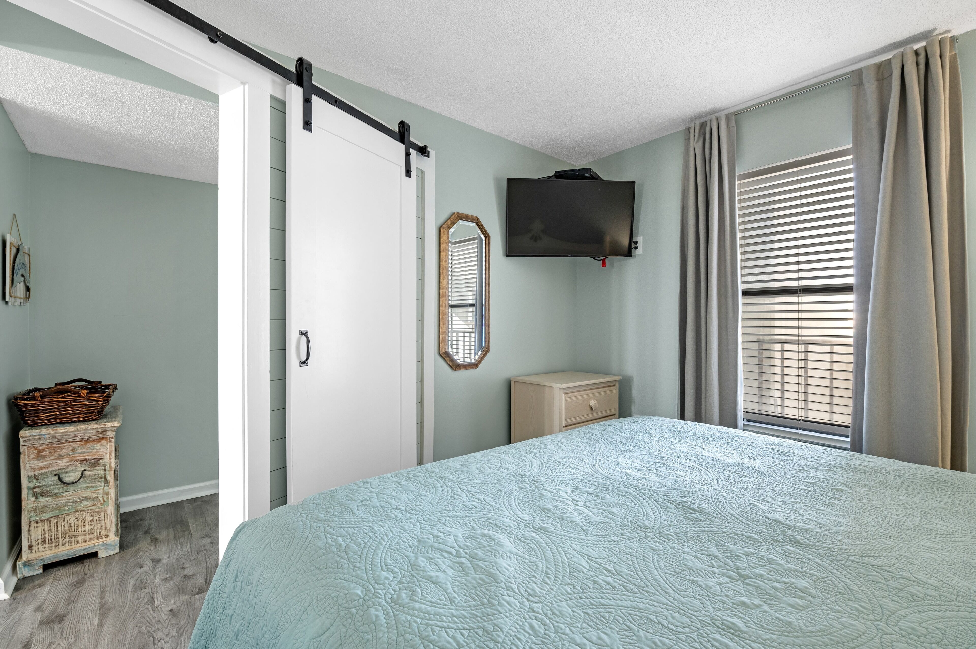 A bedroom with a bed, a dresser, a television, and a window with curtains.