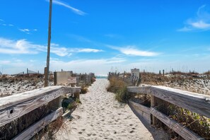 A sandy beach path with wooden railings and signs, leading towards the ocean.