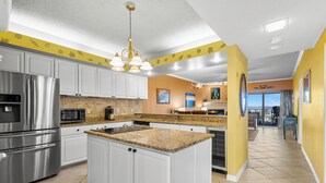 Una cocina moderna con armarios blancos, encimeras de granito, electrodomésticos de acero inoxidable y una isla central.