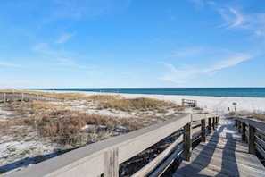 A wooden boardwalk leading to a sandy beach with a clear blue sky.