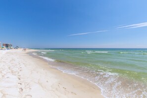Ein Strand mit blauem Himmel, sanften Wellen und Fußspuren im Sand.