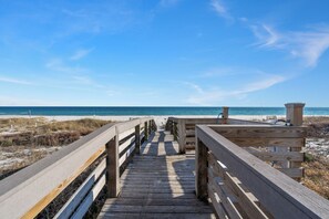 Un paseo marítimo de madera que conduce a una playa bajo un cielo azul despejado.