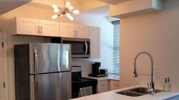 A modern kitchen with a stainless steel refrigerator, a microwave, and a built-in oven. There is a white countertop island with a sink and a pendant light above it. - FAB Studio Near Capitol, Hospitals, & Fair Grounds (Jackson)