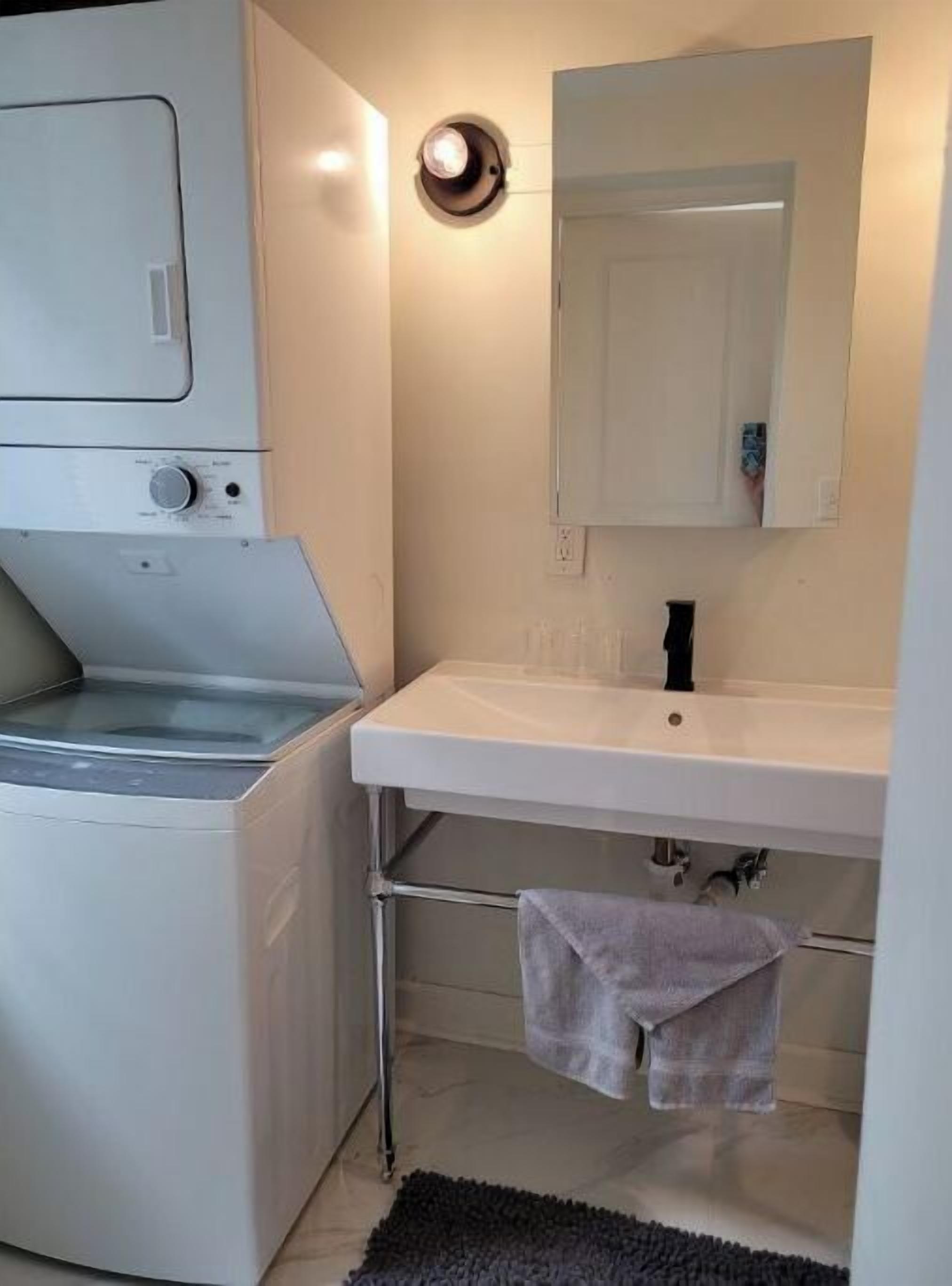 Une petite salle de bain équipée d’un lave-linge, d’un lavabo et d’un miroir.