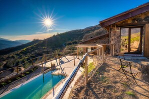 A pool with a wooden deck and a stone wall, overlooking a mountainous landscape. - Cerrás Sustainable and 100% Self-Sufficient Agrotourism TR-CC-00429 (Jerte)