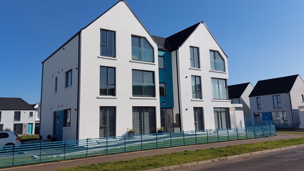A modern two-story residential building with a flat roof, large windows, and a blue door.