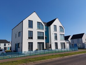 A modern two-story residential building with a flat roof, large windows, and a blue door.