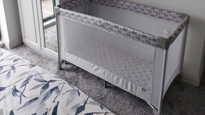 A room with a white wardrobe, a crib with a patterned mattress, and a bed with a leaf-patterned cover.