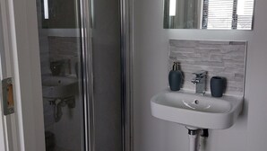 A modern bathroom with a glass shower enclosure, a white sink with two soap dispensers, and a mirror above the sink.