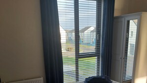 A bedroom with a bed, a radiator, and a view of a residential area through a window with curtains.