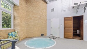 A pool area with a brick wall, a wooden door, and a bench with a patterned cushion. - Rockford Retro Revival • Indoor Pool + Arcade Fun! (Rockford)