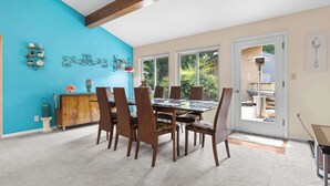 A dining area with a wooden table and chairs, a blue accent wall, and a view through a glass door. - Rockford Retro Revival • Indoor Pool + Arcade Fun! (Rockford)