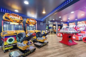 Arcade machines, a red gaming table, and a wooden floor in a room.