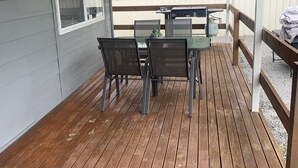 A covered outdoor patio with a wooden deck, a table with chairs, and a grill.