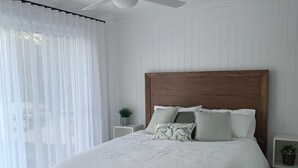 A bedroom with a large bed, white bedding, a wooden headboard, and a small bedside table with a plant.