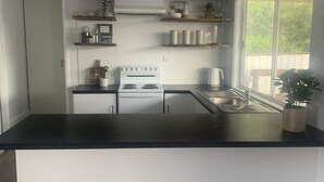 A modern kitchen with white cabinetry, a black countertop, and a built-in stove. There are shelves above the stove holding decorative items and plants.