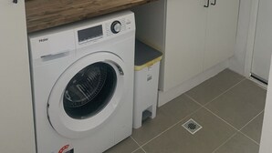A compact kitchen with a built-in washer and dryer, a wooden countertop, a sink, and a window with a view of greenery.