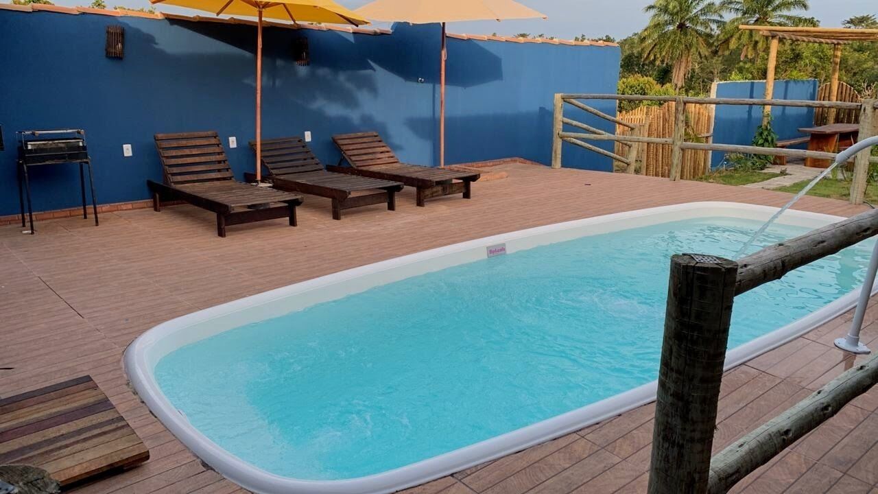 Piscina con tumbonas de madera y sombrillas, rodeada por un muro azul y una terraza de madera.