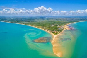 An aerial view of a coastal area with clear turquoise waters, sandy beaches, and a small settlement with visible roads and buildings. - Casas Araras de Corumbau-piscina 5 Min da Praia (Prado)