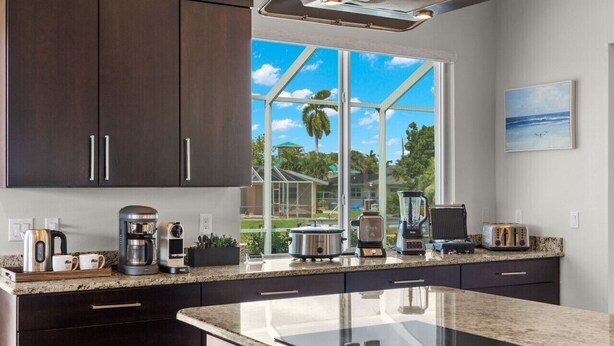A modern kitchen with dark cabinets, a large window, and various appliances. - Luxury home w/ 2 suites, LARGE pool, spa, lanai. Quick gulf access! 6 Bikes! EV! (Cape Coral)
