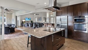 A spacious kitchen with a large island, stainless steel appliances, and a dining area with modern furniture. - Luxury home w/ 2 suites, LARGE pool, spa, lanai. Quick gulf access! 6 Bikes! EV! (Cape Coral)