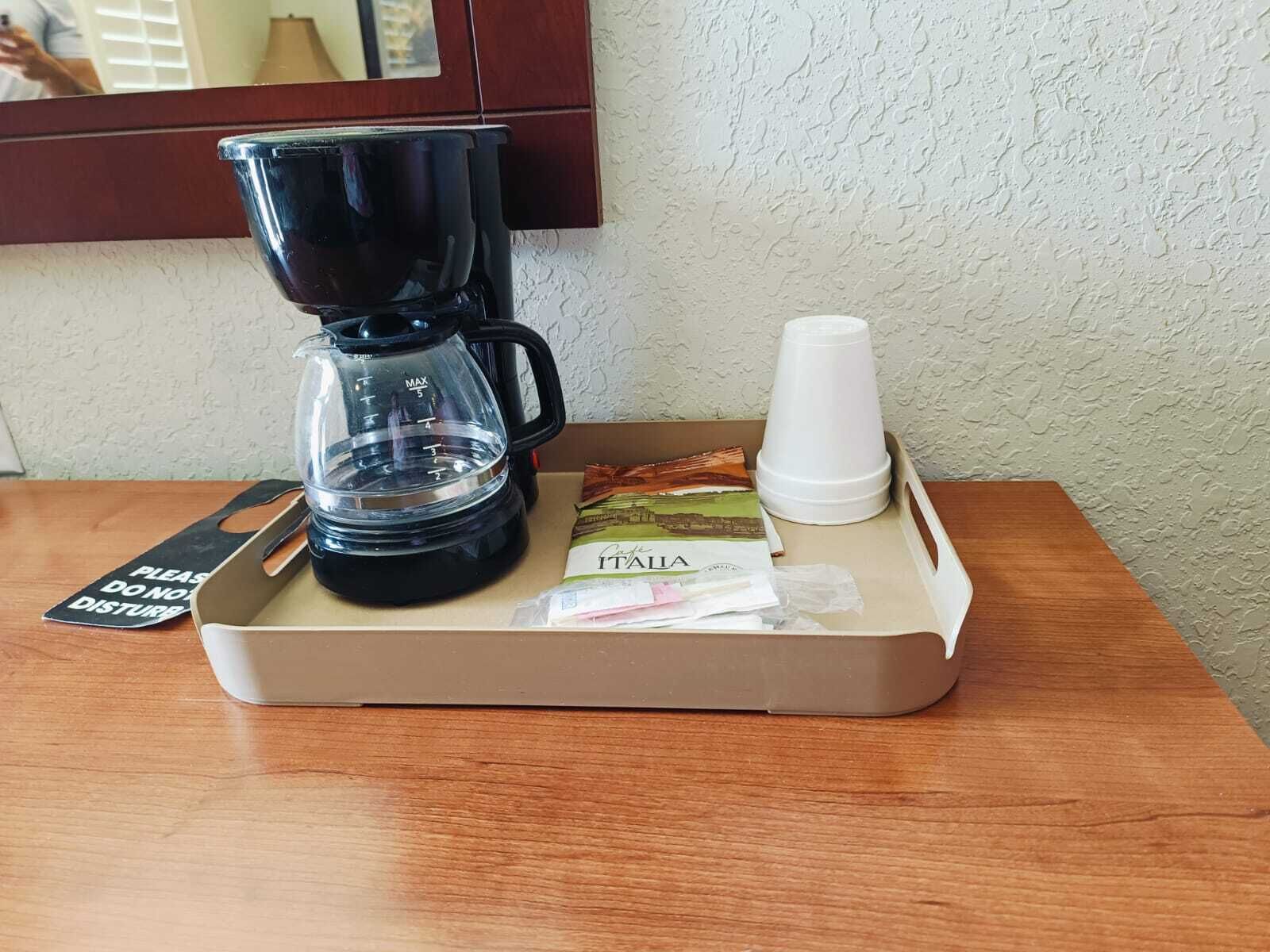 A tray with a coffee maker, a cup, a packet of tea, and a napkin on a wooden table.