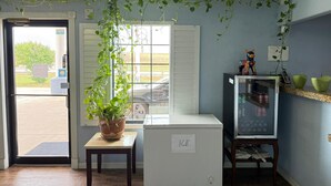 A room with a white refrigerator labeled "ICE," a small table with a potted plant, a glass display case with a price tag, and a door leading outside. - Hotel O Bien Venido Pearsall I-35 (Pearsall)