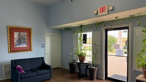 A lobby with a blue couch, a framed picture, potted plants, an exit sign, and a door leading outside. - Hotel O Bien Venido Pearsall I-35 (Pearsall)