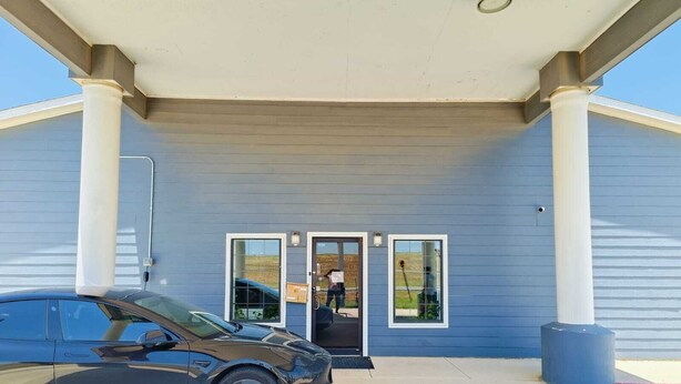 A building with a covered entrance, a car parked in front, and a person entering through the door. - Hotel O Bien Venido Pearsall I-35 (Pearsall)