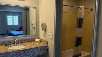 A bathroom with a granite countertop sink, a mirror, a hairdryer, and a shower curtain.