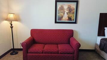 A red patterned sofa in a room with a lamp and a framed painting on the wall.