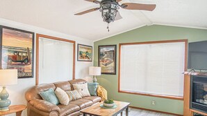 A living room with a brown leather sofa, a wooden coffee table, a ceiling fan, and framed artwork on the walls. - Meadowview Clean & Comfortable Home by River Side (Klamath)