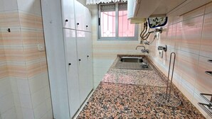 Une cuisine avec des meubles blancs, un plan de travail en granit, un évier et une fenêtre ornée d’un rideau en dentelle.