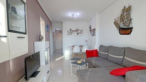Un salon moderne avec un canapé gris, un téléviseur à écran plat et un coin repas à l’arrière-plan.