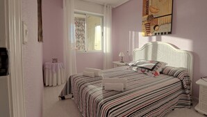 Une chambre à coucher comprenant un lit, une table de chevet, une lampe, une fenêtre avec des rideaux et un ventilateur de plafond.