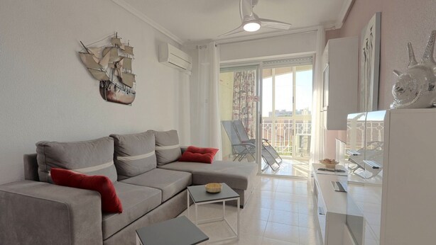 Un salon moderne avec un canapé d’angle gris, une petite table et un balcon équipé d’une chaise.