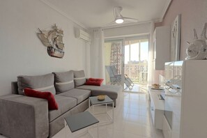 Ein modernes Wohnzimmer mit einem grauen Ecksofa, einem kleinen Tisch und einem Balkon mit einem Sessel.