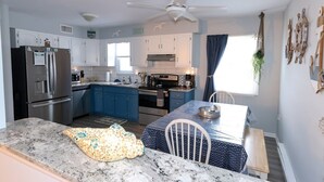 A modern kitchen with white cabinets, a stainless steel refrigerator, and a dining area with a blue tablecloth. - Newly remodeled 3 BR, 2 Bath shore house sleeps 10. (Wildwood Crest)