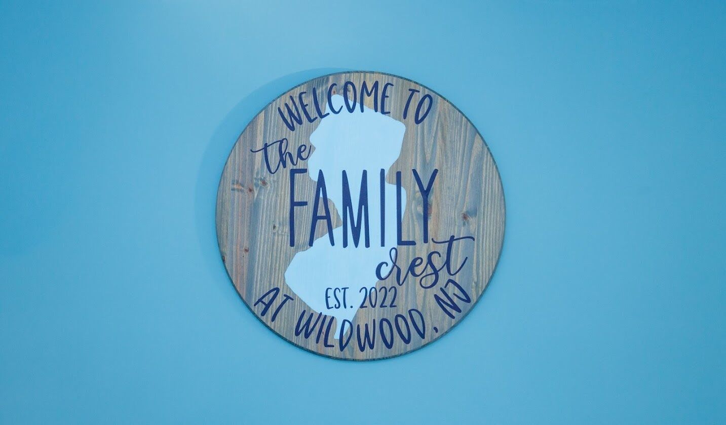 A circular wooden sign with the text "WELCOME TO the FAMILY" and "EST. 2022 AT WILDWOOD, NJ".