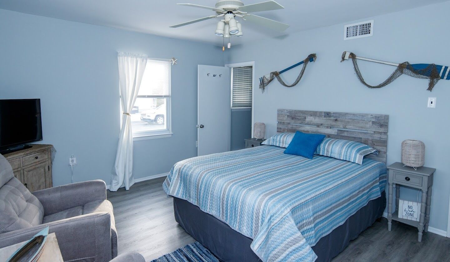 A bedroom with a bed, a TV, a chair, a nightstand, and a ceiling fan.