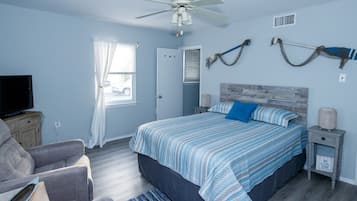 A bedroom with a bed, a TV, a chair, a nightstand, and a ceiling fan.