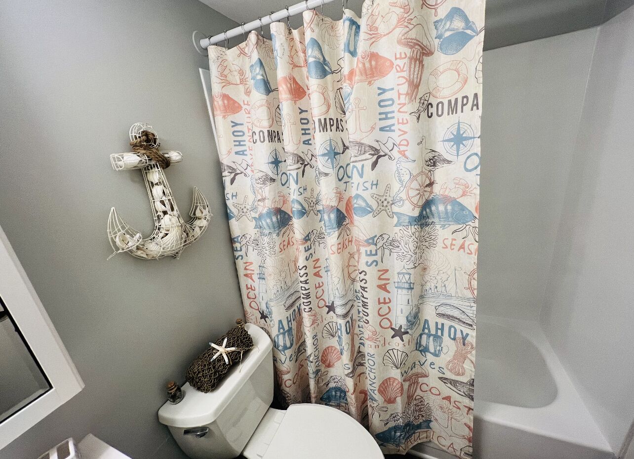 A bathroom with a nautical-themed shower curtain, a white toilet, and a wall-mounted decorative anchor.