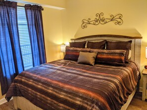 Een net opgemaakt bed met een gestreept deken, een hoofdbord met een decoratief metalen ontwerp, en een raam met blauwe gordijnen.