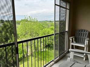 Enjoy the serene view from this balcony, featuring a comfortable Adirondack chair and a sliding glass door.